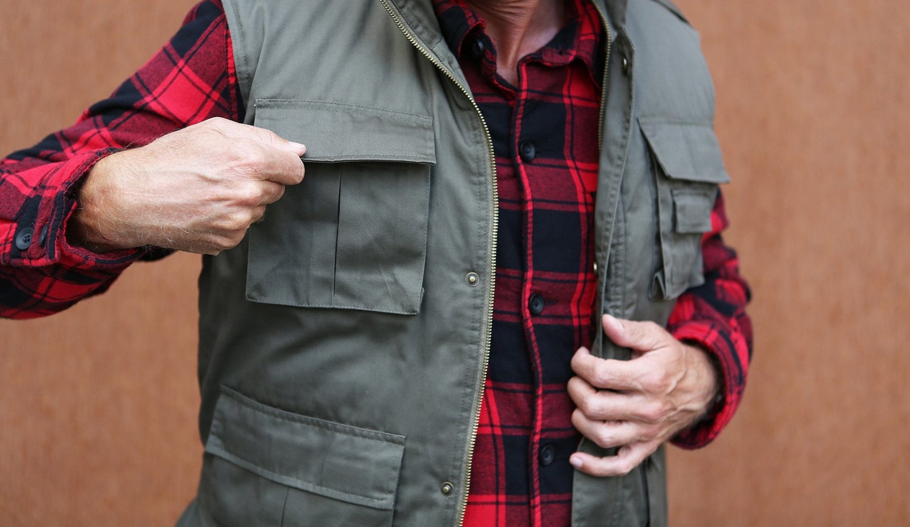 Person wearing a green vest over a red and black plaid shirt against a brown background