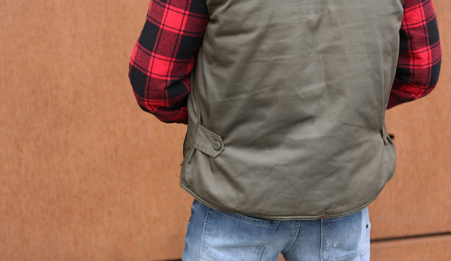 Person wearing a green vest over a red and black plaid shirt with a brown background