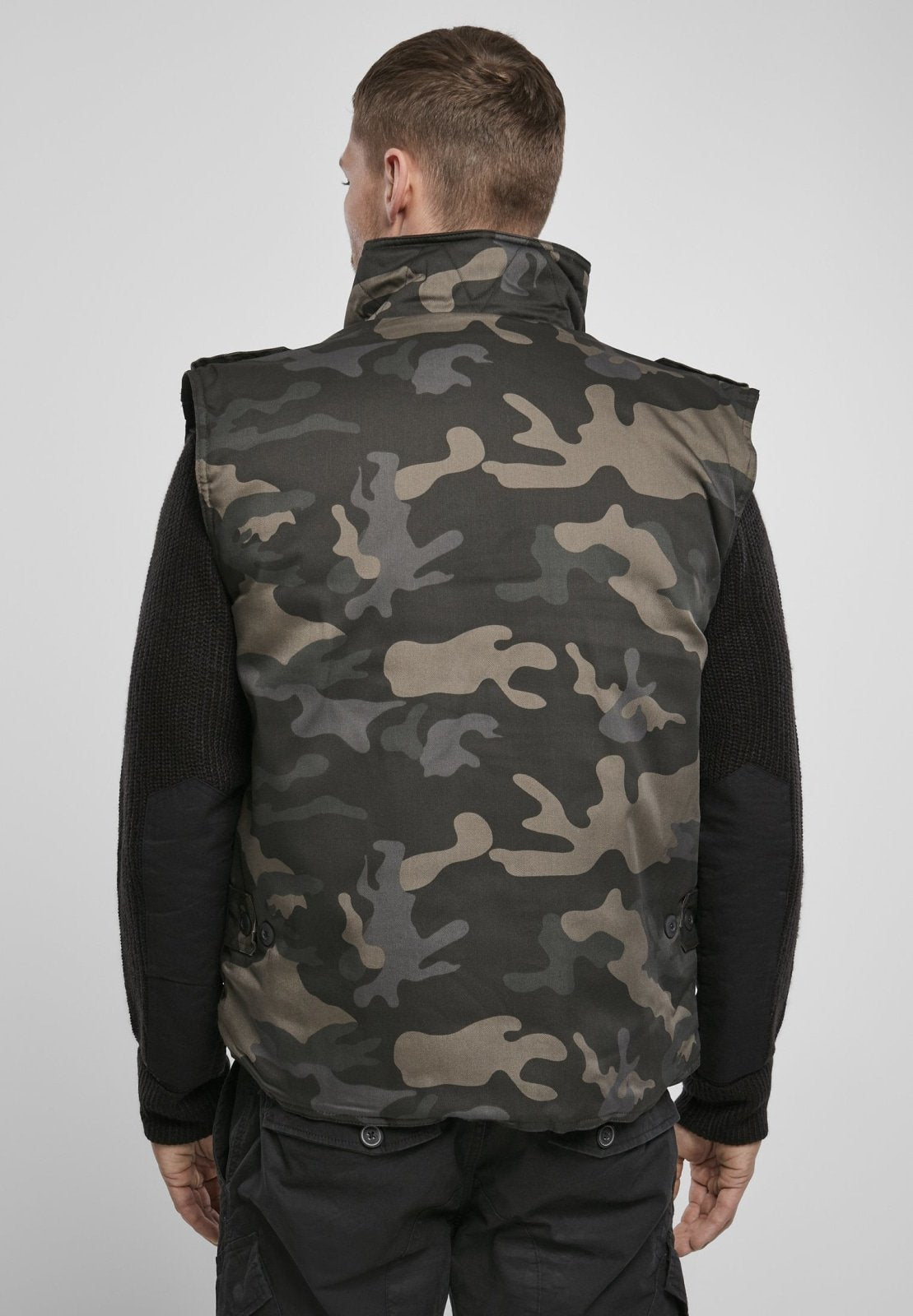 Person wearing a camouflage vest over a black shirt on a white background