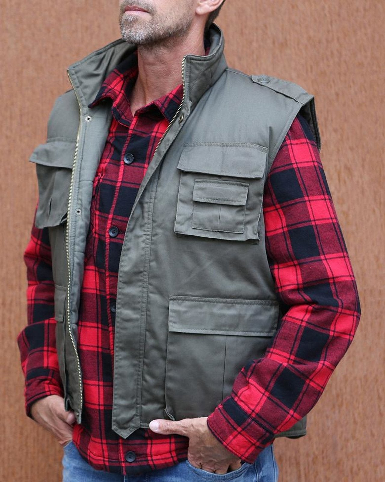 Man wearing a red and black plaid shirt with a green vest against a brown background