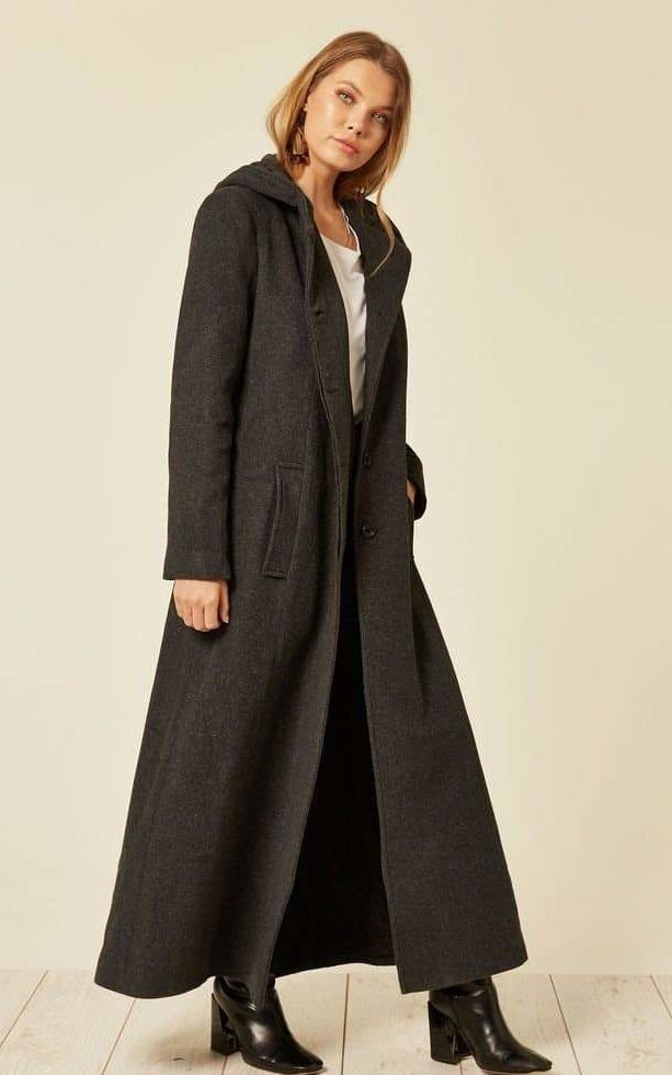 Woman wearing a long dark coat on a plain background