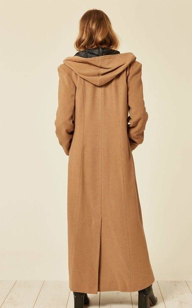 Person wearing a long brown coat with a hood on a plain background