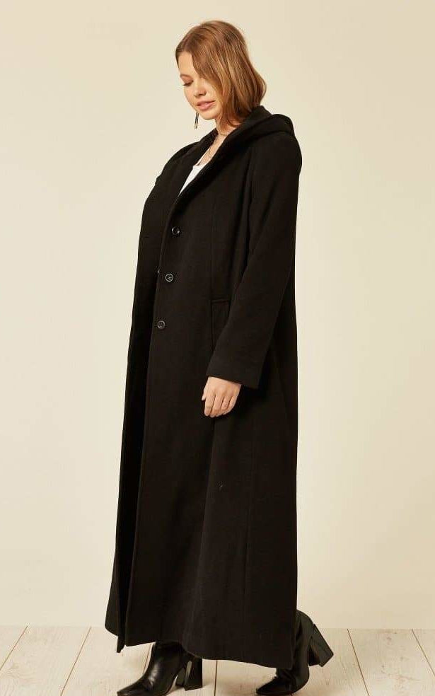 Woman wearing a long black coat on a plain background