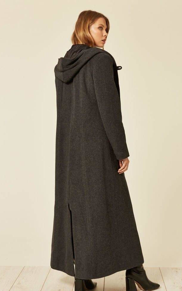 Woman wearing a long dark coat on a plain background