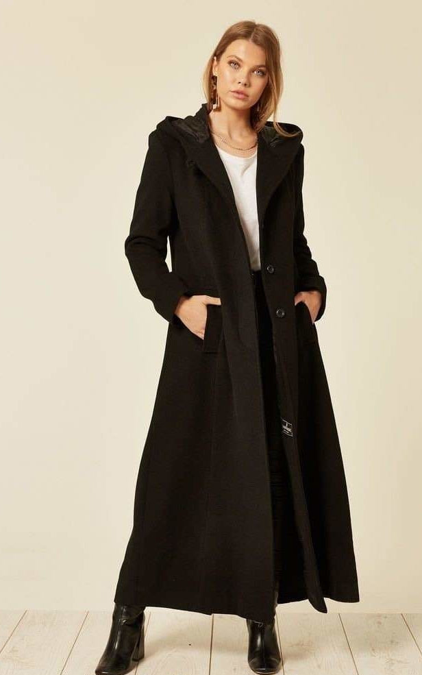 Woman wearing a long black coat on a plain background