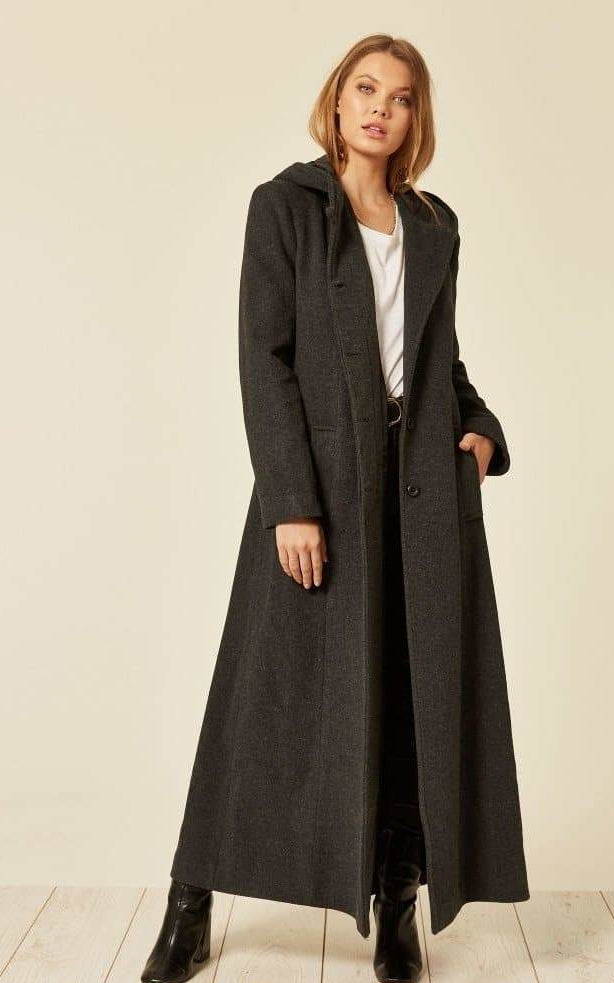 Woman wearing a long dark coat on a plain background