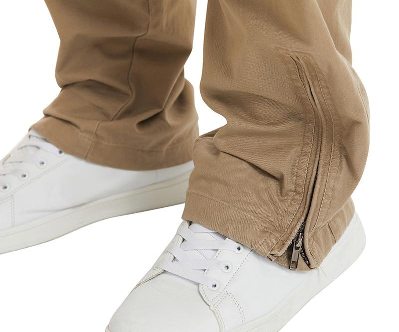 Brown pants with a zipper detail worn with white sneakers on a white background