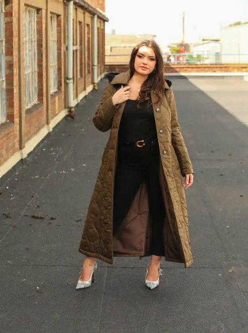 Woman wearing a long brown coat on a rooftop with a building in the background