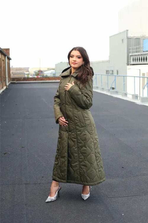 Woman wearing a long green quilted coat on a rooftop.