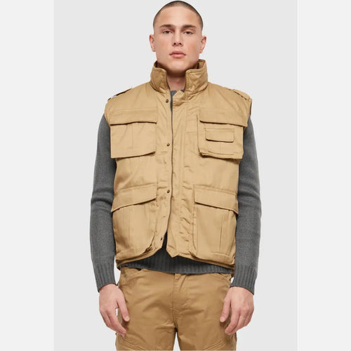 Man wearing a beige vest over a gray sweater on a white background