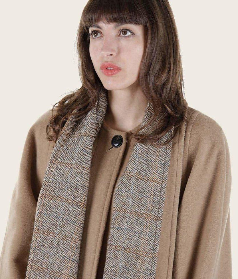 Woman wearing a beige coat with a patterned scarf against a plain background
