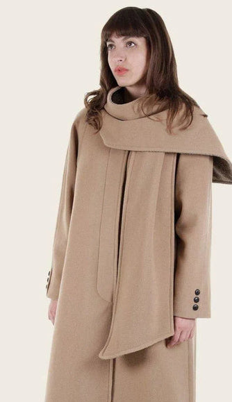 Woman wearing a beige coat with a large collar, standing against a white background.