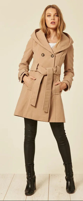 Woman wearing a beige coat with a belt, standing against a plain background.