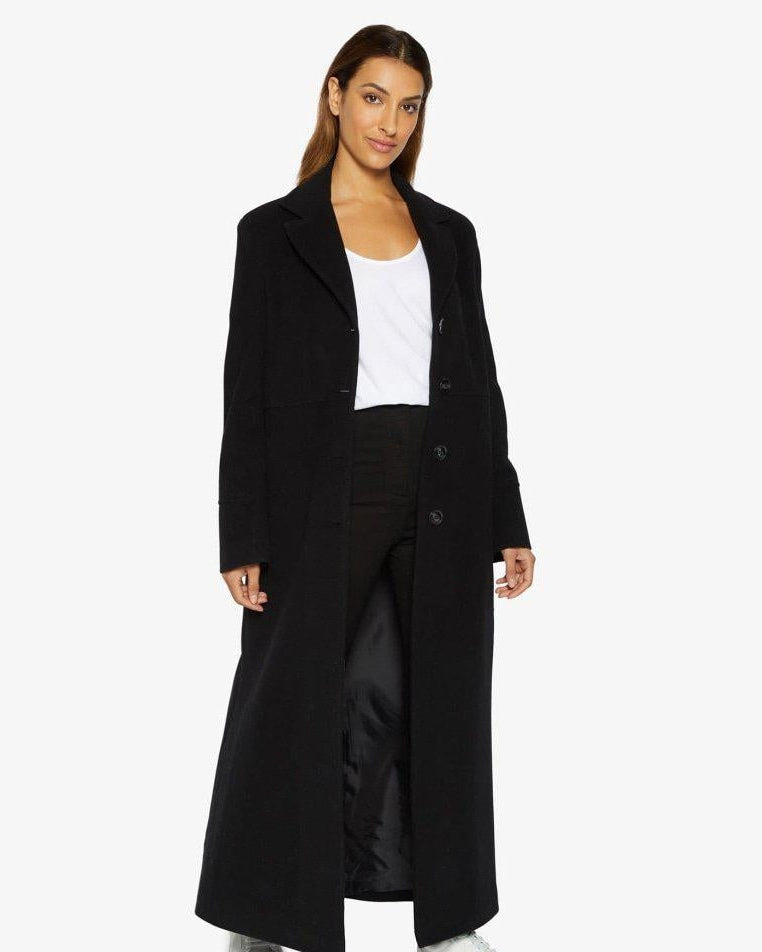 Woman wearing a long black coat over a white top on a white background