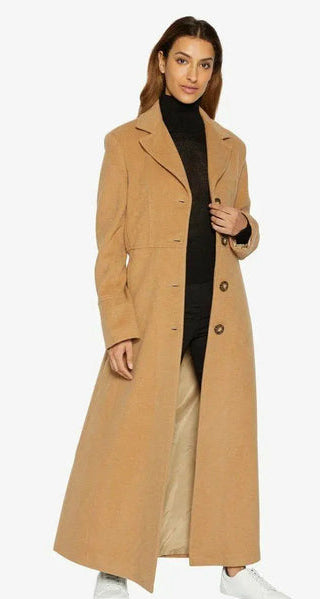 Woman wearing a long beige coat with a black turtleneck and white pants, on a white background