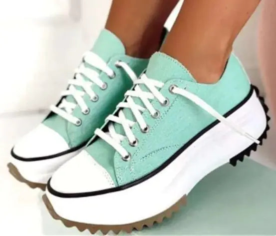 Teal sneakers with white soles worn by a person on a light background