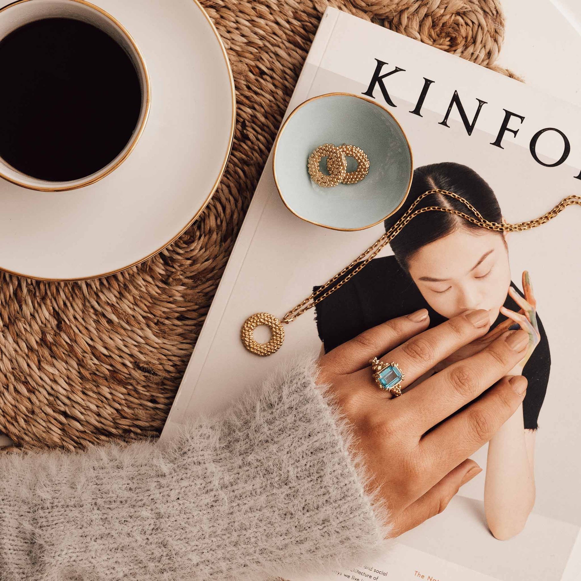 Close-up of a magazine with jewelry and a cup of coffee on a textured surface