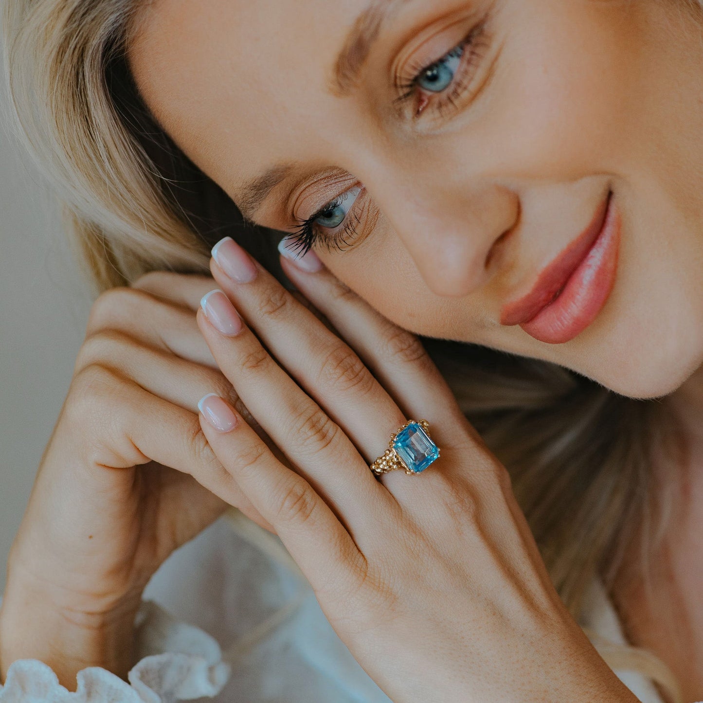 Woman wearing a gold ring with a blue gemstone, close-up of hand and face.