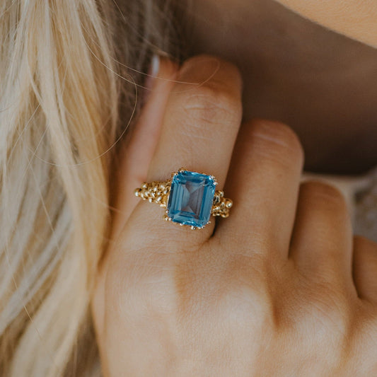 Close-up of a hand wearing a gold ring with a blue gemstone.