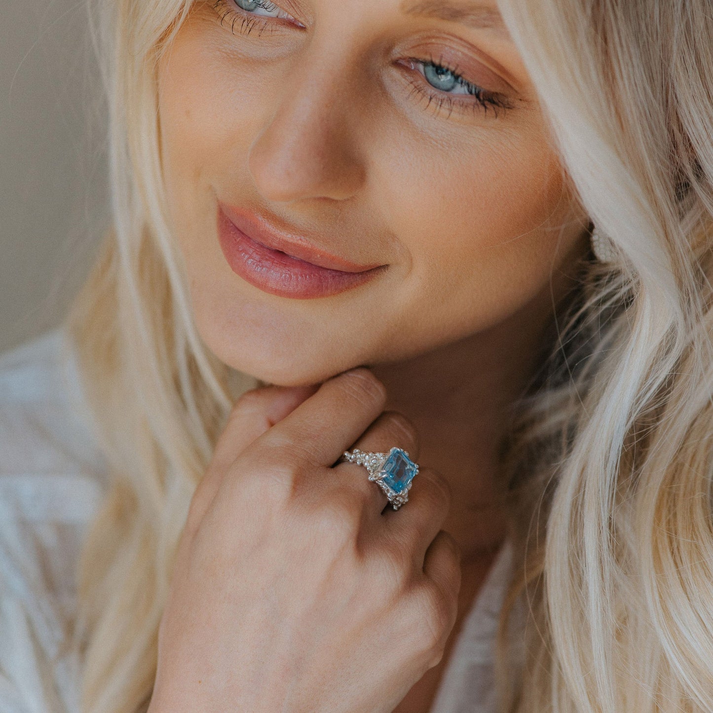 Close-up of a woman wearing a ring with a blue gemstone, against a neutral background.