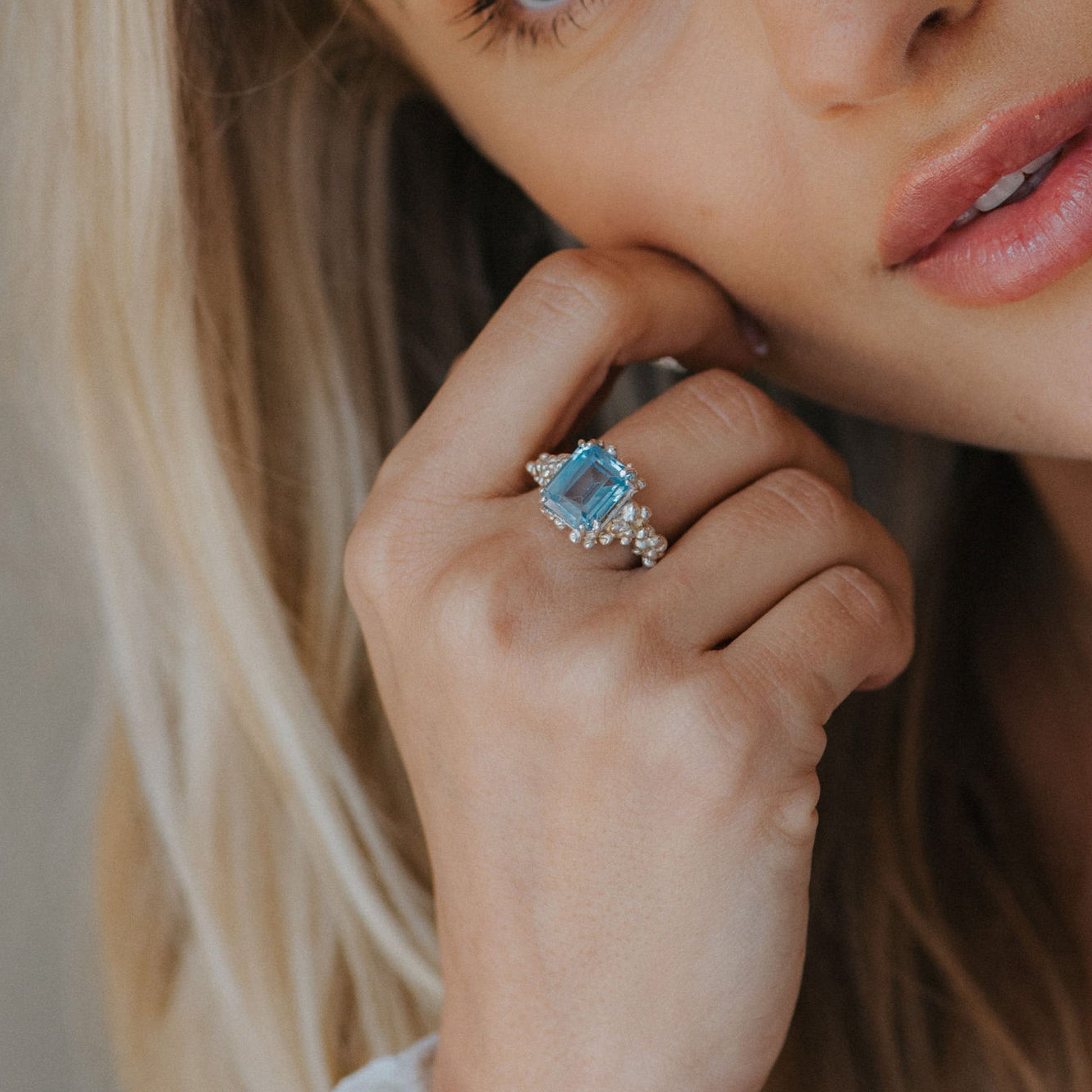Close-up of a woman's hand wearing a blue gemstone ring with a blurred background