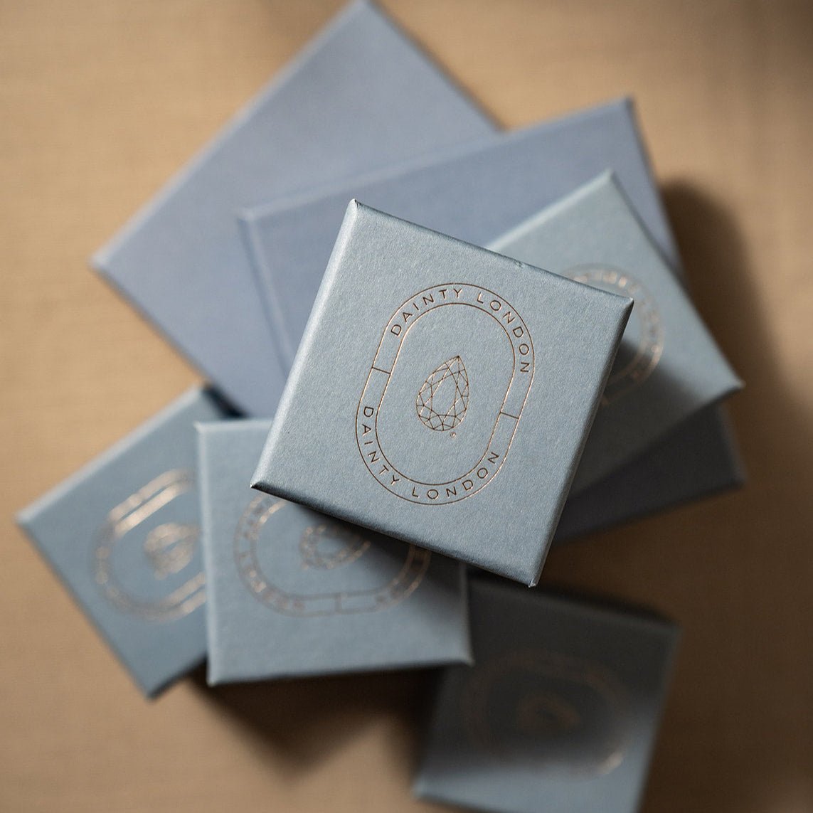 Stack of light blue boxes with 'Dainty London' branding on a beige background