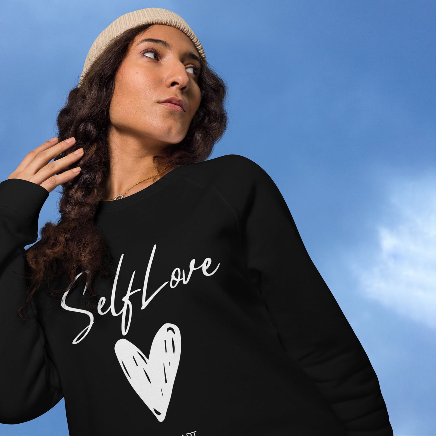 Person wearing a black sweatshirt with 'Self Love' and a heart design against a blue sky.