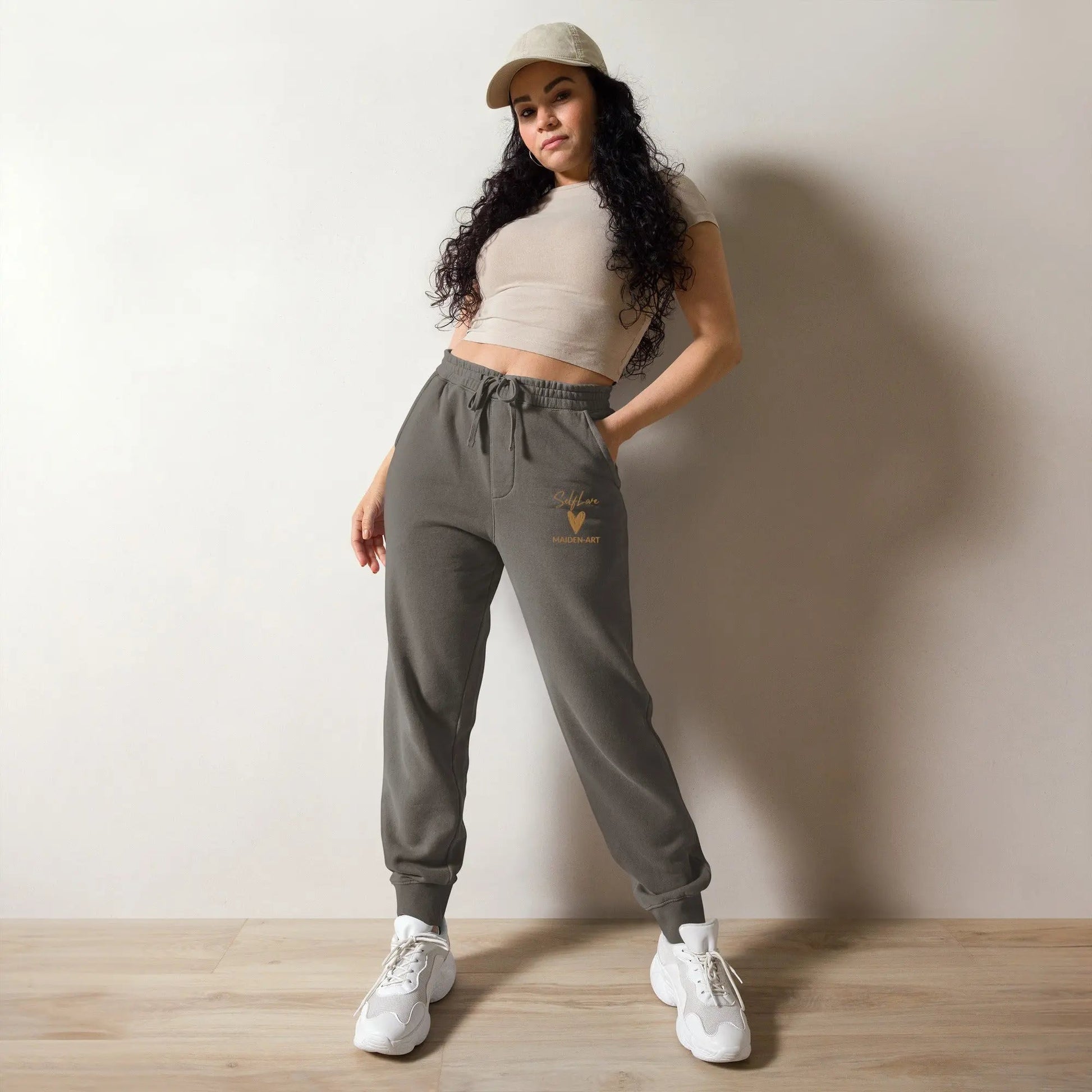 Woman wearing a beige crop top, gray sweatpants, and white sneakers against a plain wall.