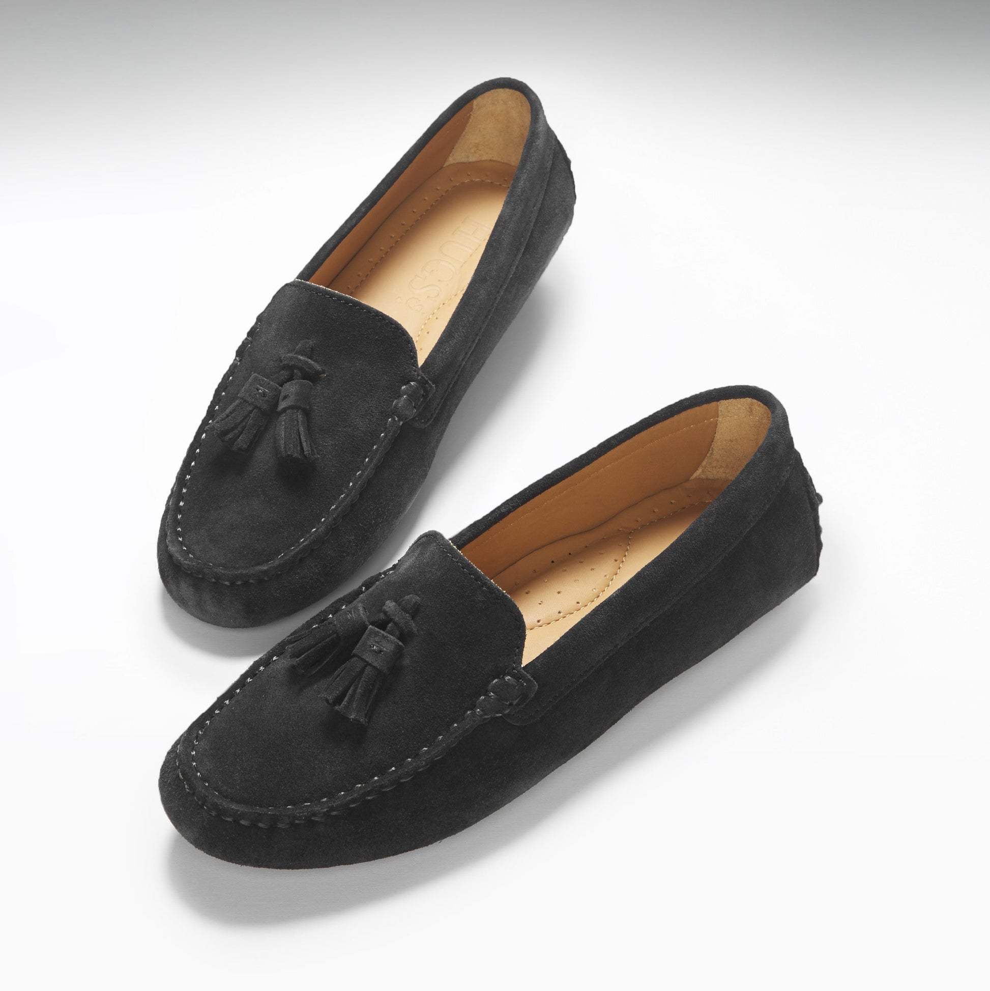 Pair of black suede loafers with tassels on a white background