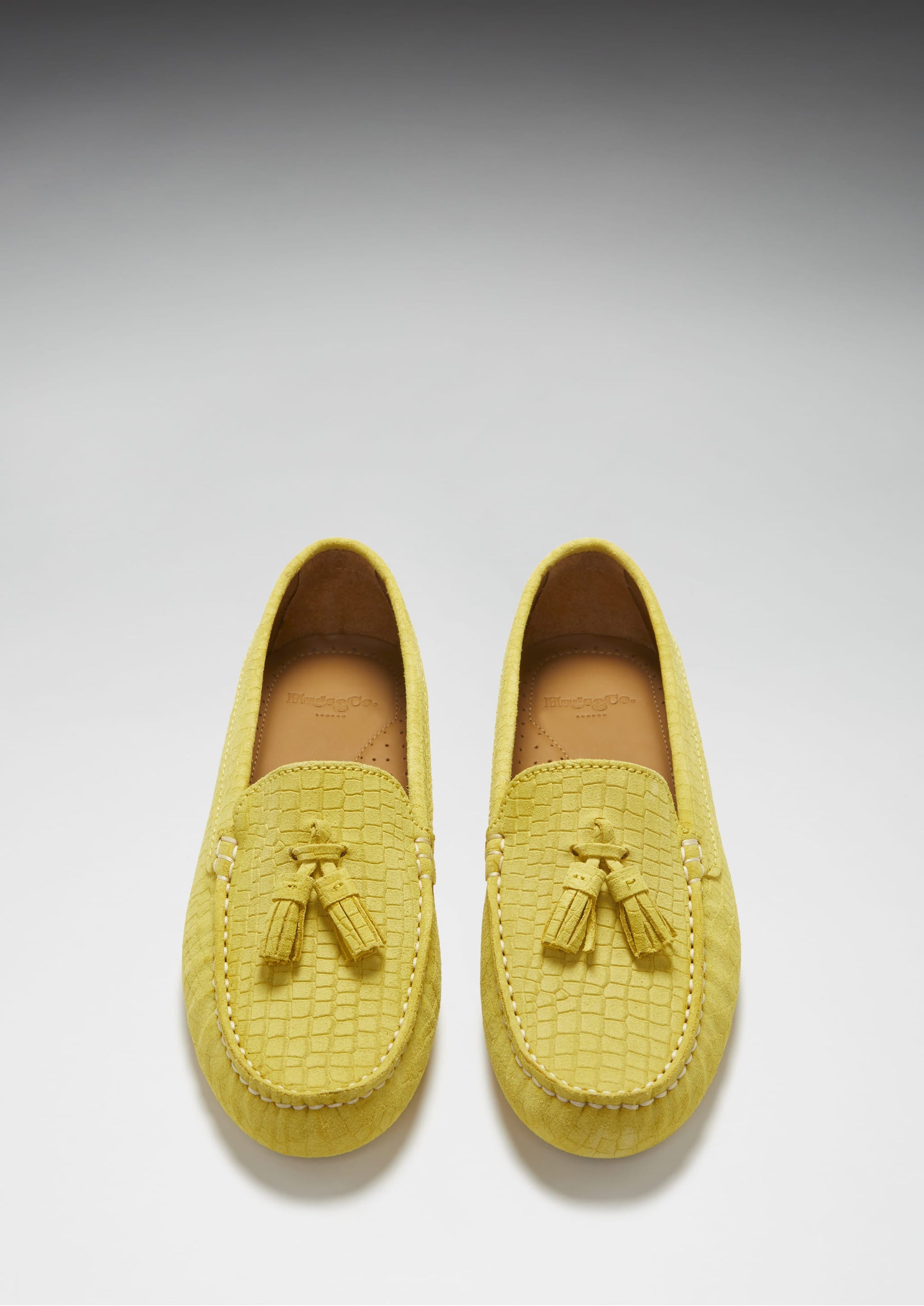 Pair of yellow loafers with tassel details on a light gray background