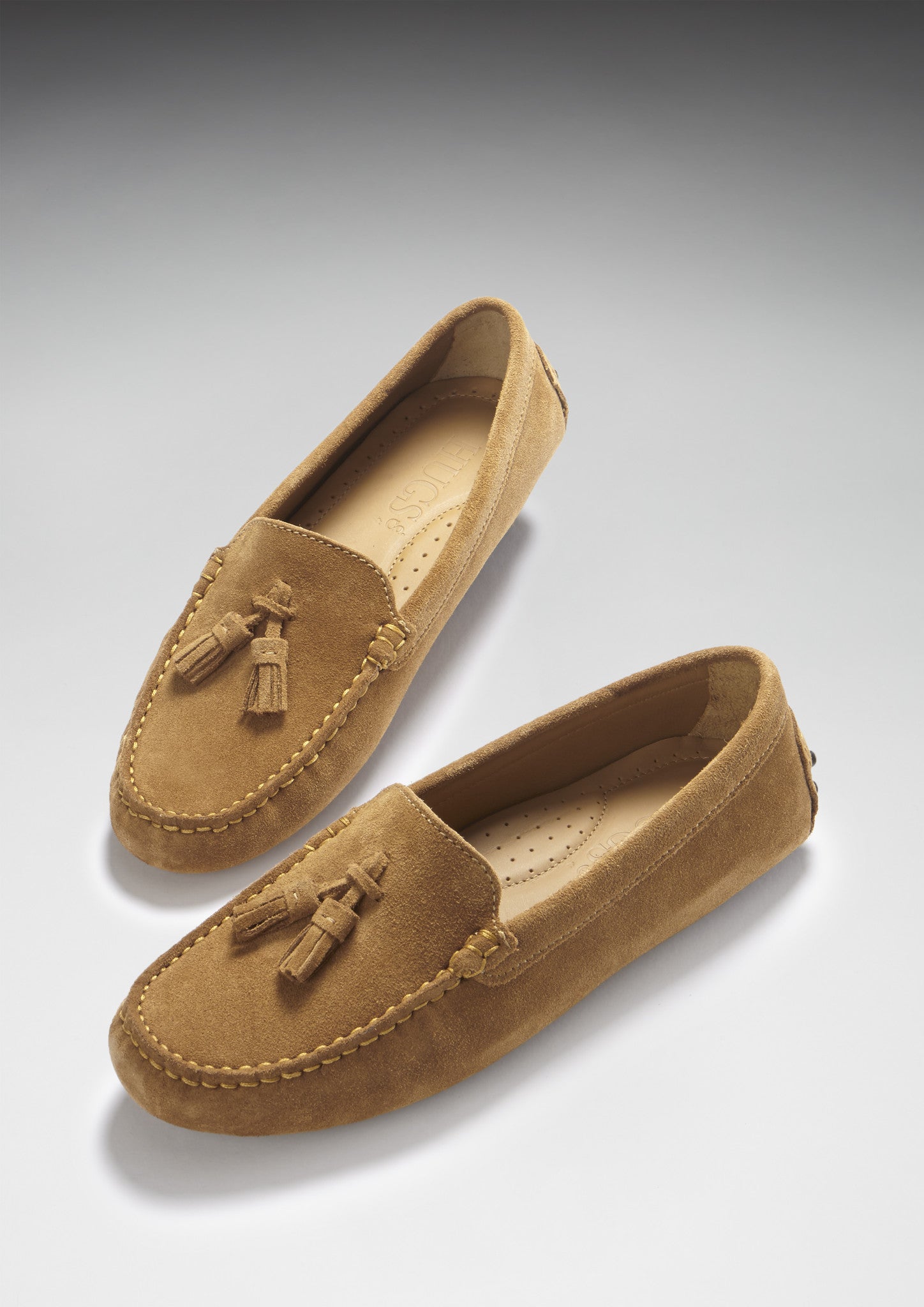 Pair of tan loafers with tassels on a light gray background