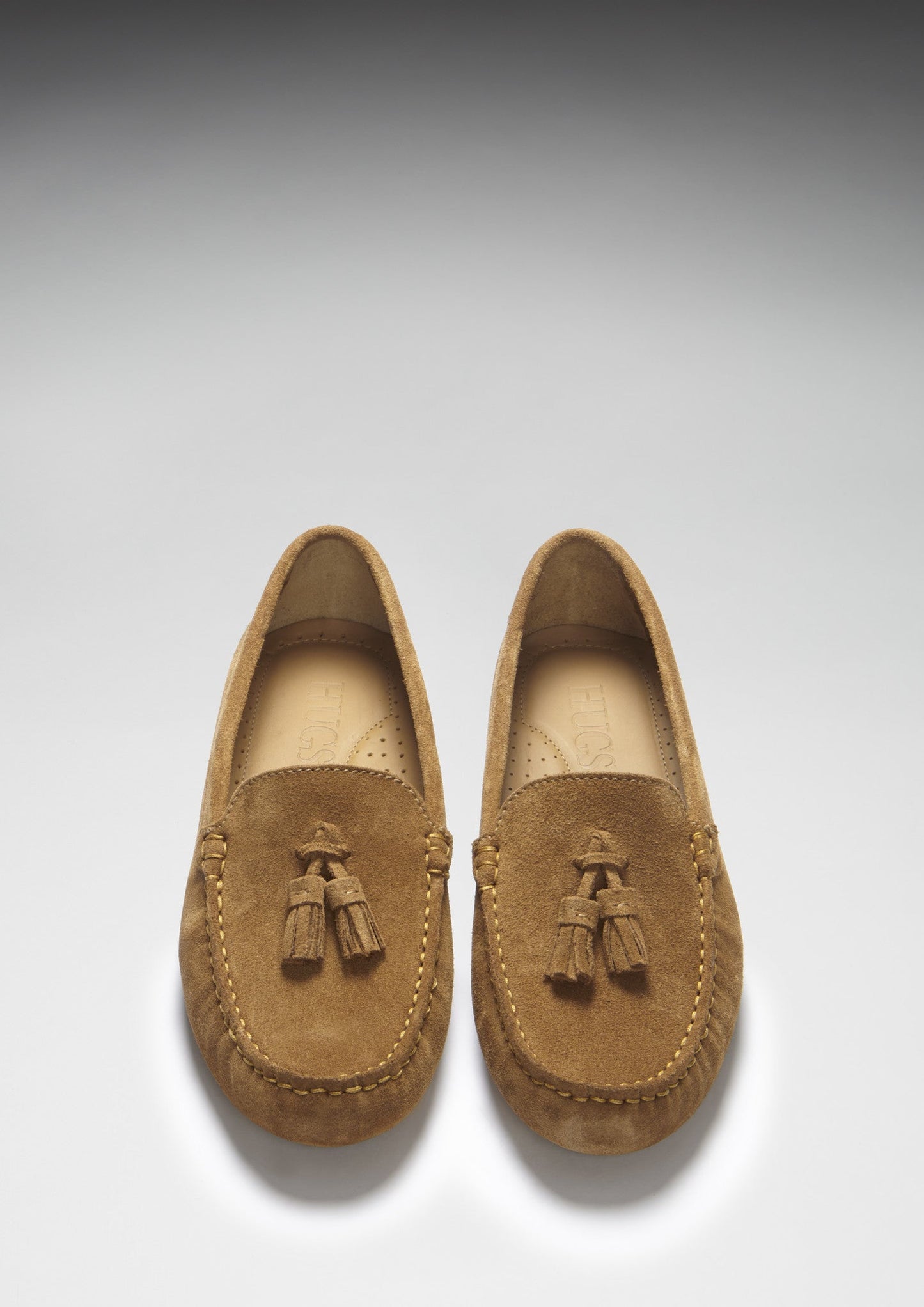 Pair of brown suede loafers with tassels on a light gray background