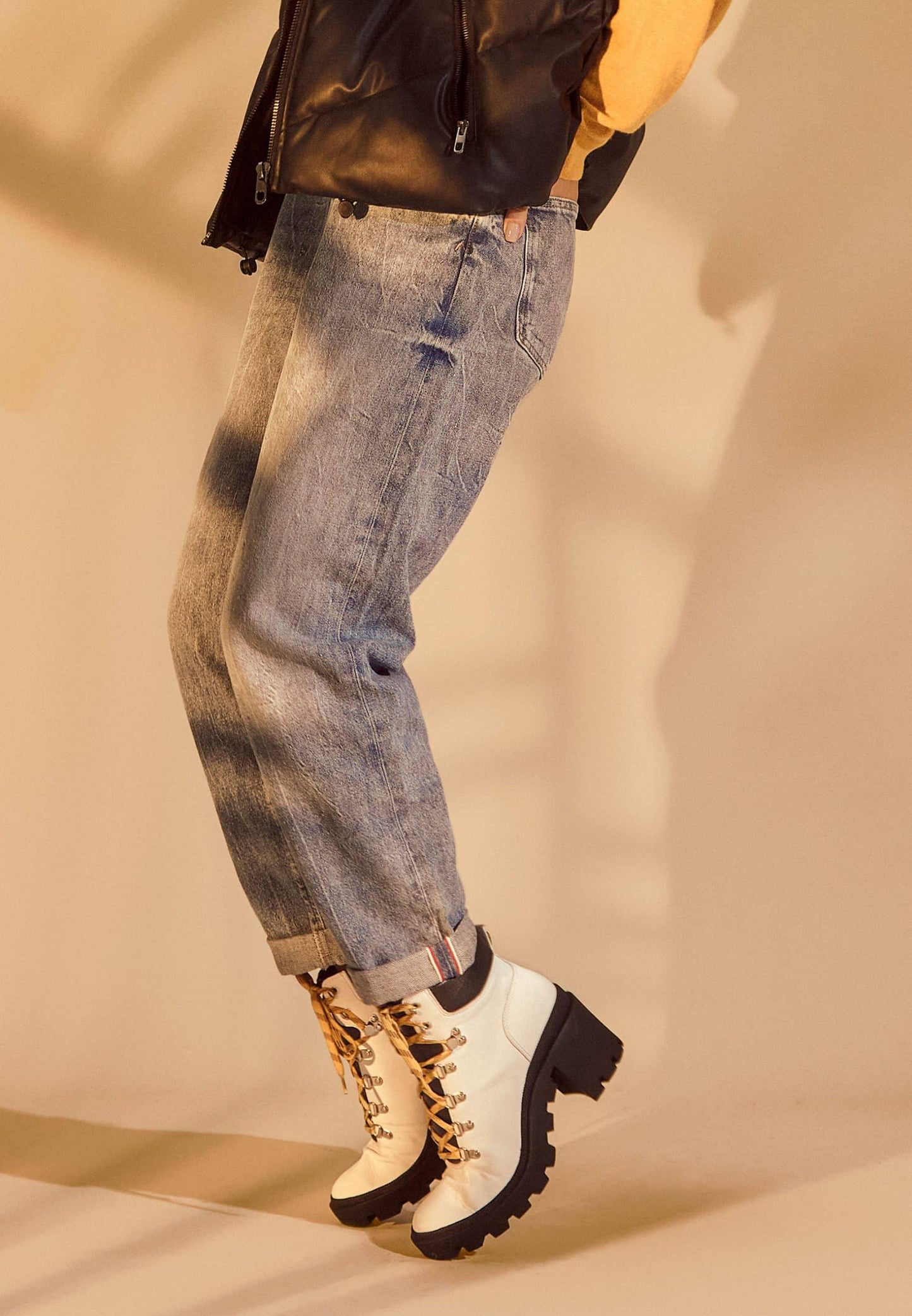 Person wearing blue jeans and white boots with black soles on a beige background