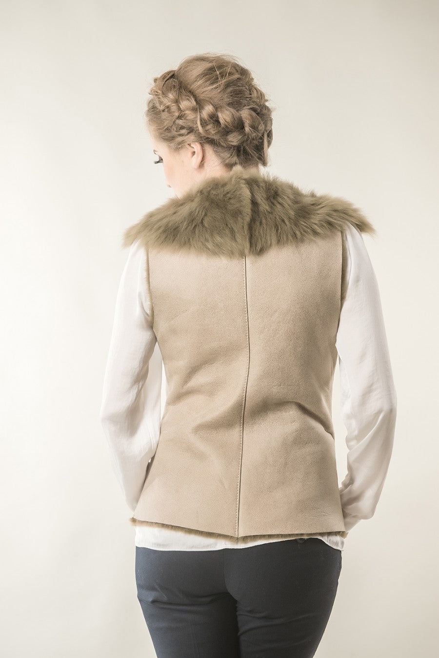 Person wearing a beige vest with fur collar on a plain background