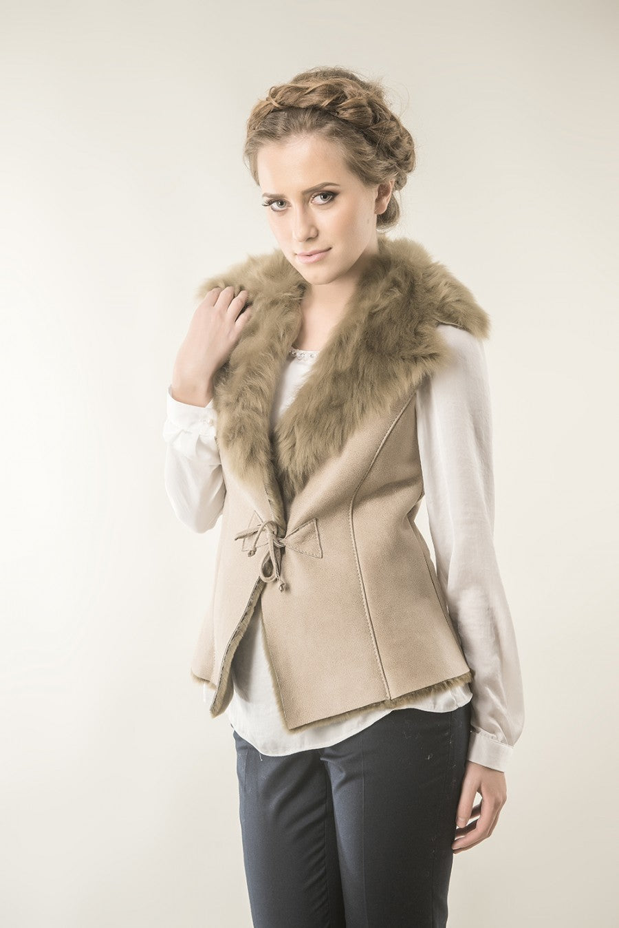 Woman wearing a beige vest with fur collar against a plain background