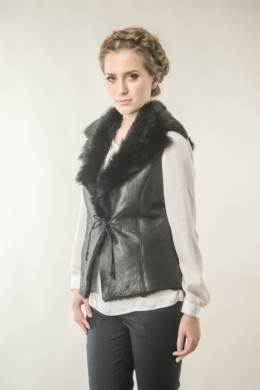 Woman wearing a black leather vest with fur collar against a plain background