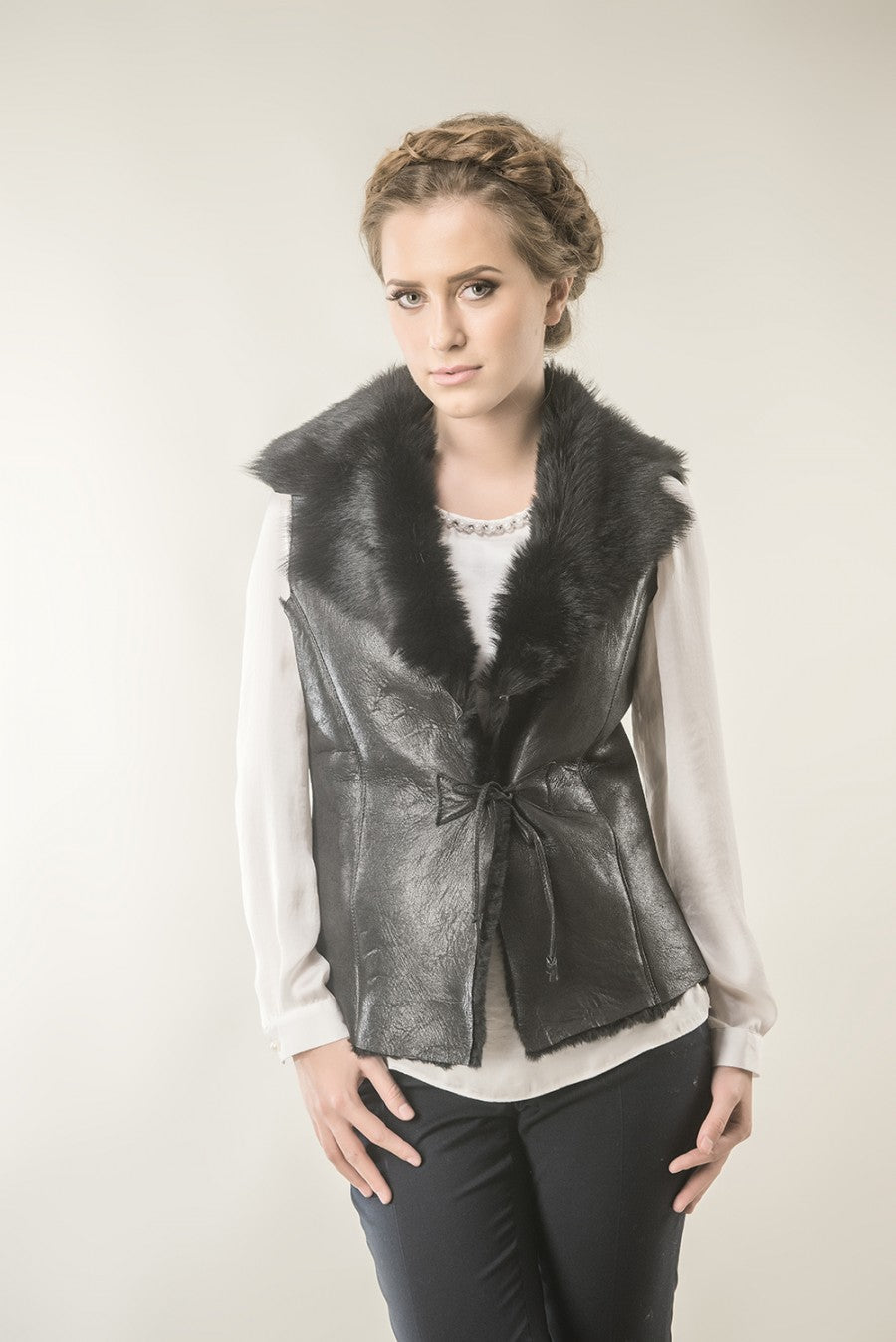 Woman wearing a black leather vest with fur collar against a plain background