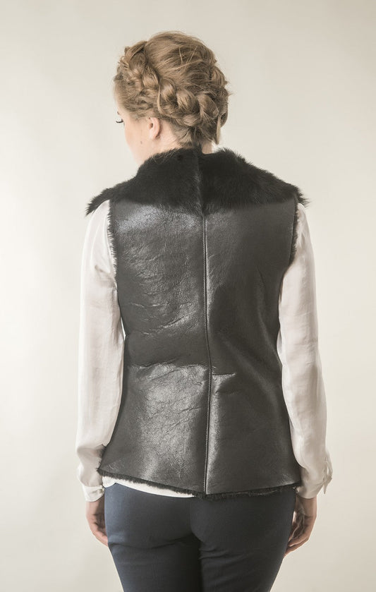 Person wearing a black leather vest with fur trim on a plain background