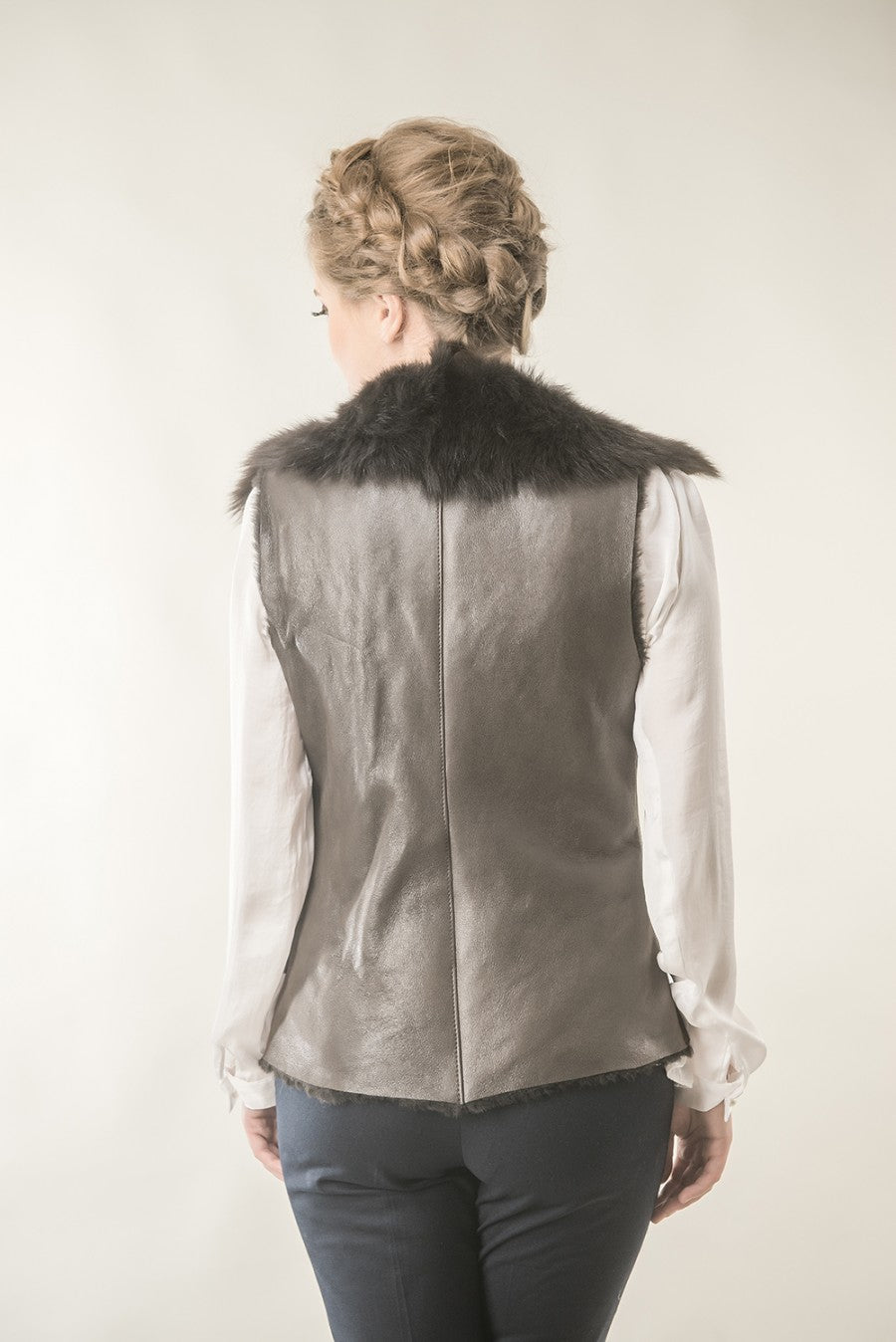 Person wearing a gray leather vest with fur collar on a plain background