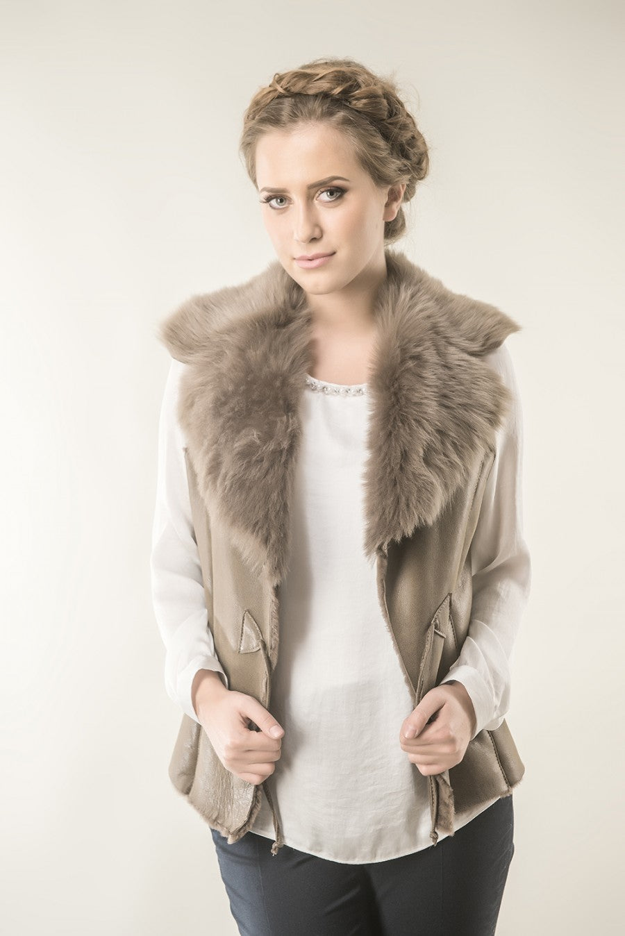 Woman wearing a beige vest with fur collar against a plain background