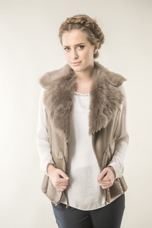 Woman wearing a beige vest with fur collar against a plain background