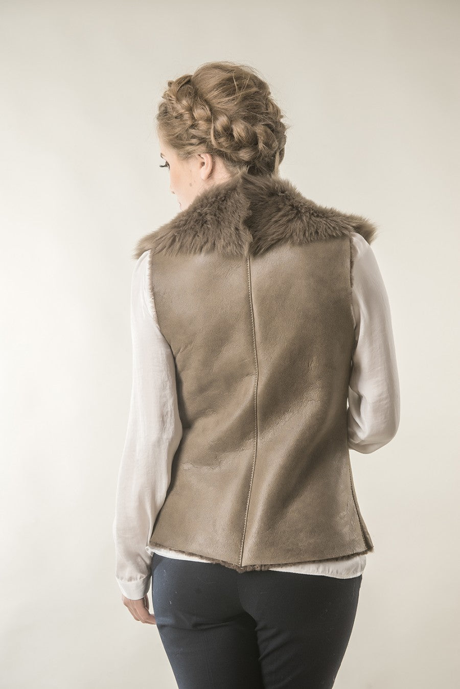 Person wearing a brown leather vest with fur collar on a plain background