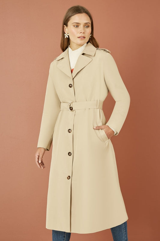 Woman wearing a beige trench coat against a brown background