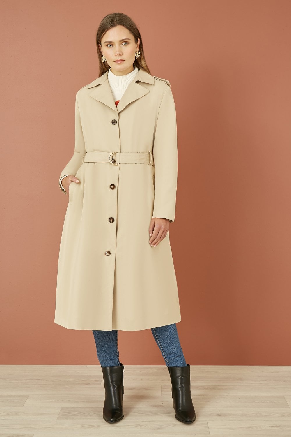 Woman wearing a beige coat with a belt against a brown background