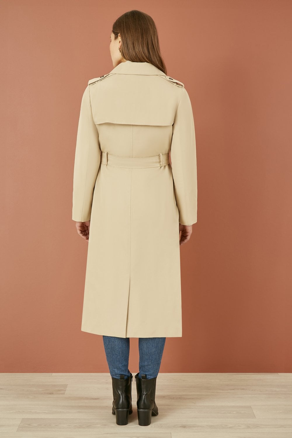Woman wearing a beige trench coat against a brown background