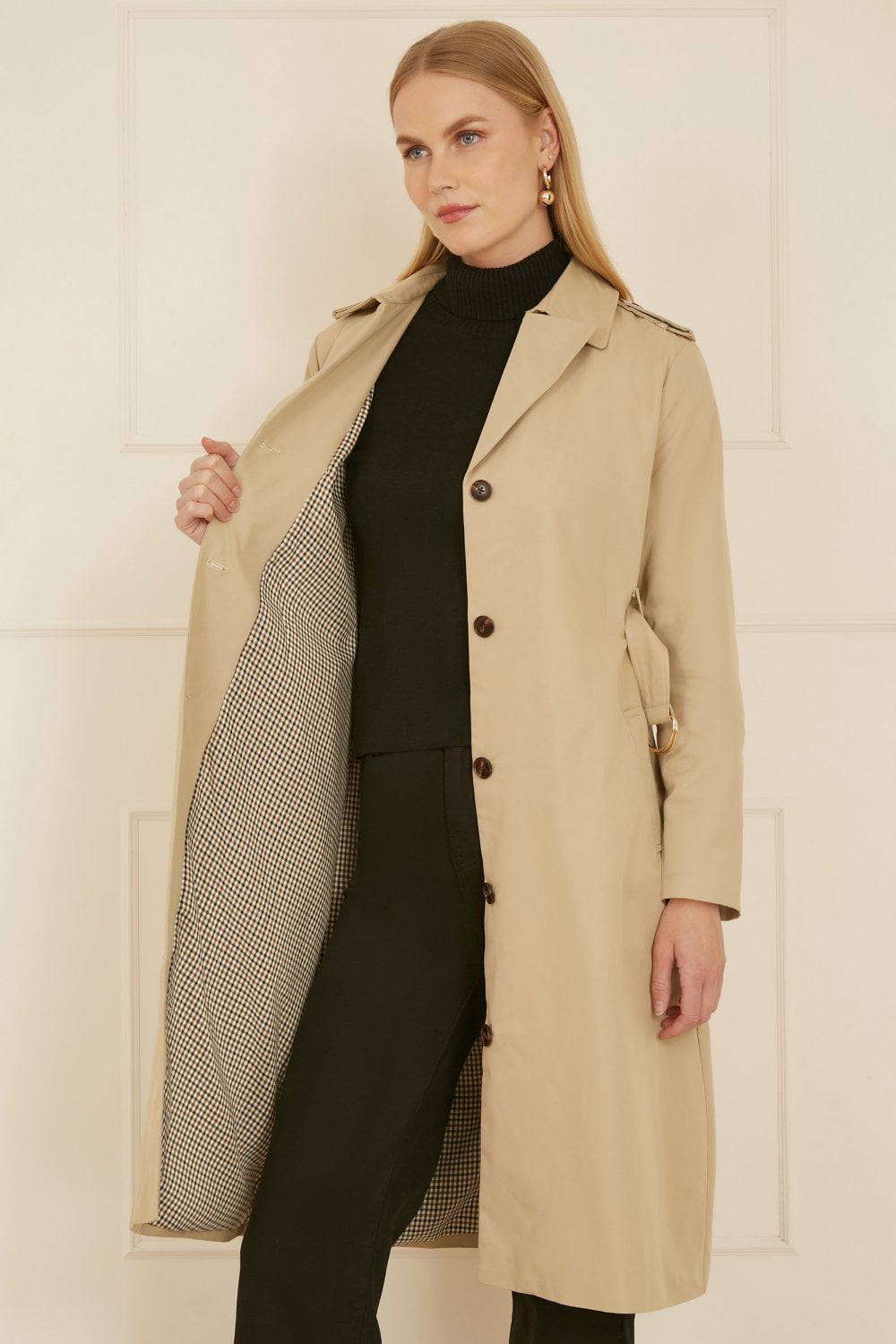 Woman wearing a beige trench coat over a black outfit against a white background