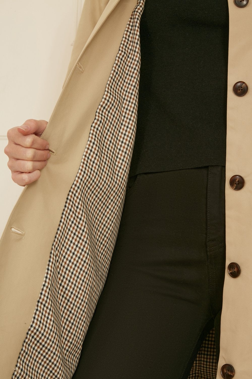 Close-up of a beige coat with a checkered lining and black buttons.