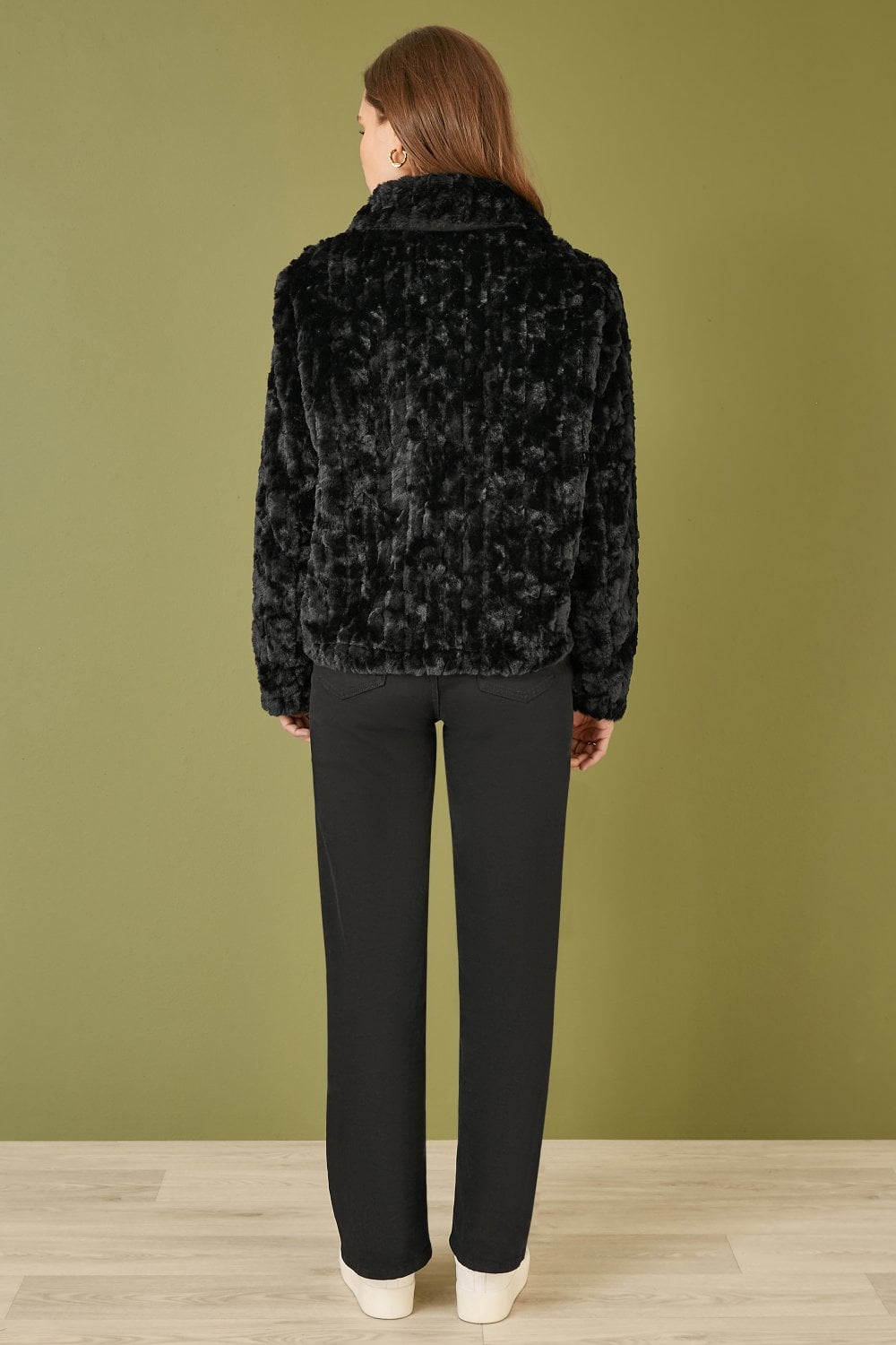 Person wearing a black leopard print jacket against a green wall