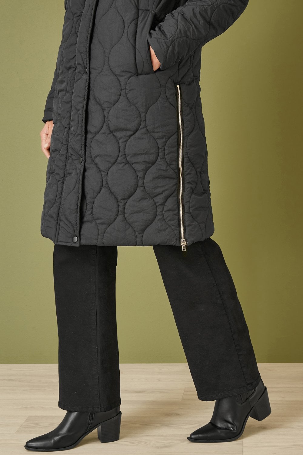 Person wearing a black quilted coat with a green background