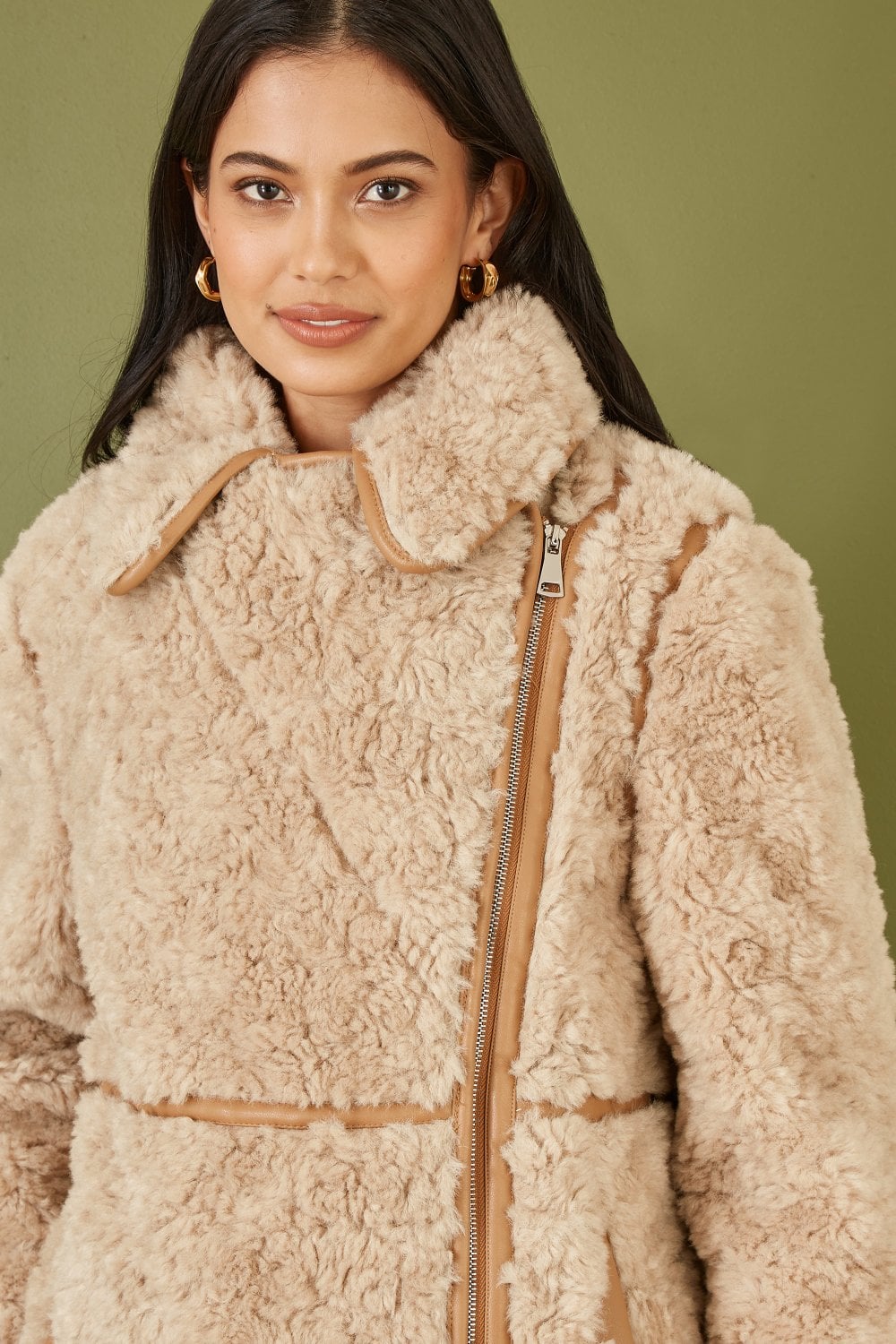 Woman wearing a beige sherpa jacket with a zipper on a green background